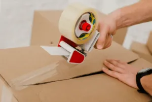 Un ragazzo che sigilla uno scatolone con un dispenser nastro Un ragazzo che sigilla uno scatolone con un dispenser nastro
