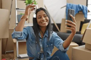 Una ragazza sorridente che, seduta per terra in una stanza con tutti scatoloni, mostra al telefono un mazzo di chiavi