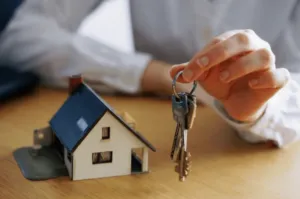 Una ricostruzione in miniatura di una casa con una ragazza che tiene in mano le chiavi di un'abitazione