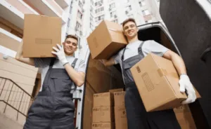 Due traslocatori che sollevano degli scatoloni vicino al loro furgone carico Due traslocatori che sollevano degli scatoloni vicino al loro furgone carico