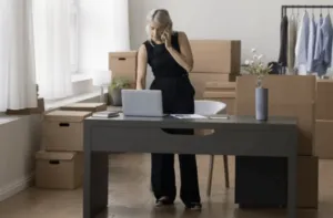 Ragazza in piedi al telefono mentre controlla il suo pc in una stanza piena di scatoloni