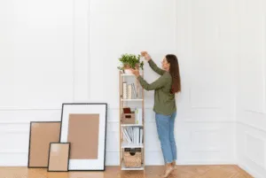 Ragazza che sistema una pianta su un mobile alto con dei quadri vuoti al lato Ragazza che sistema una pianta su un mobile alto con dei quadri vuoti al lato