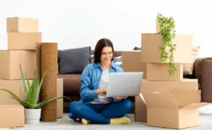 Ragazza seduta per terra, circondata da scatoloni, mentre consulta il web per un preventivo online gratuito Ragazza seduta per terra, circondata da scatoloni, mentre consulta il web per un preventivo online gratuito