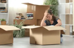 Ragazza seduta per terra mentre rammaricata controlla il contenuto di uno scatolone Ragazza seduta per terra mentre rammaricata controlla il contenuto di uno scatolone