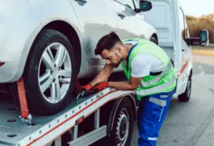 Un giovane operaio mentre lega le ruote di una macchina bianca con degli appositi ganci alla bisarca