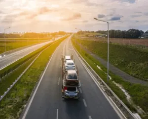 Foto dall'alto di una bisarca che trasporta un carico di macchine lungo un rettilineo immerso nel verde