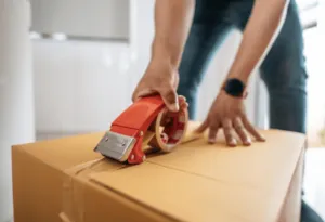 Primo piano del dispenser di nastro che viene usata da un uomo per chiudere uno scatolone Primo piano del dispenser di nastro che viene usata da un uomo per chiudere uno scatolone