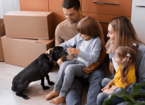 Una famiglia che coccola il loro cagnolino nero in una stanza con degli scatoloni da trasloco