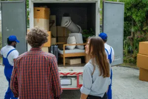 Una coppia di spalle che controlla i traslocatori che caricano mobili e scatoloni sul loro furgone Una coppia di spalle che controlla i traslocatori che caricano mobili e scatoloni sul loro furgone